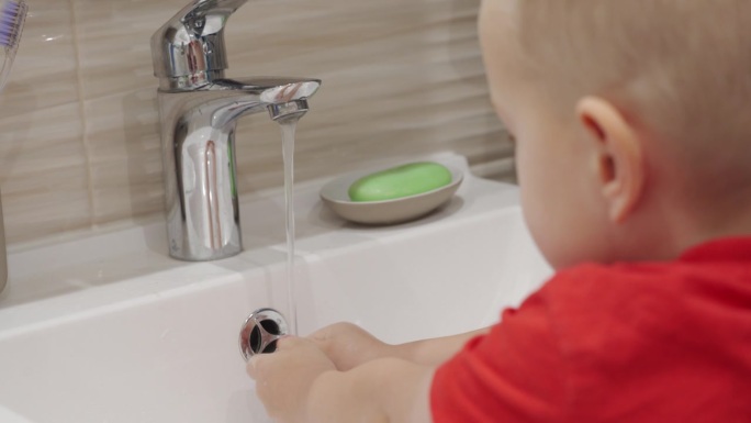3岁的孩子正在学习洗手。可爱的小男孩在水槽里用洗手液洗手。