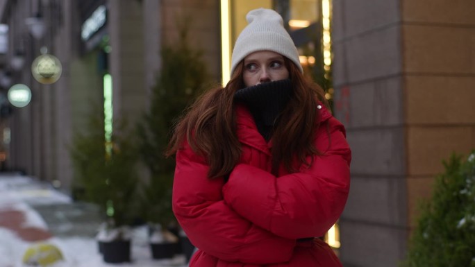 中景:在寒冷的大风天气里，穿着冬装的漂亮女子在城市街道上等出租车，她搓着手，吹着手掌取暖