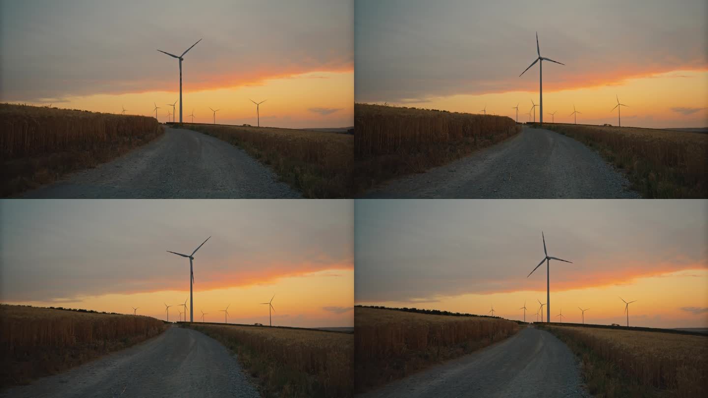 通往明天的道路:黄昏时分，麦田里的土路通往旋转的风力涡轮机