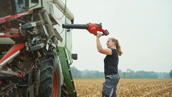 年轻的女农民在玉米收获后用吹叶机清洗联合收割机