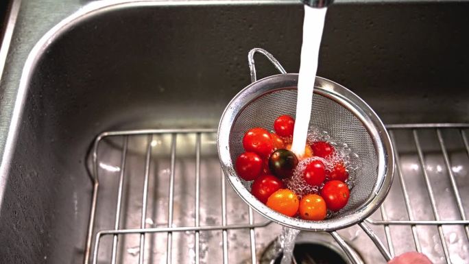 用滤网在厨房水槽里清洗新鲜的圣女果