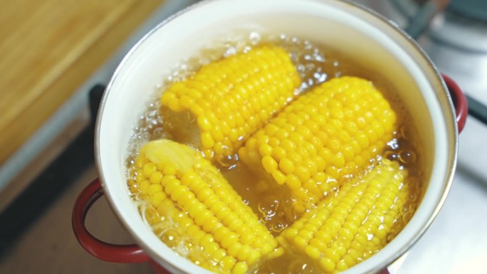 在没有水龙头的白色搪瓷平底锅里，用沸水煮黄色玉米棒的俯视图。最受欢迎的每日膳食纤维来源