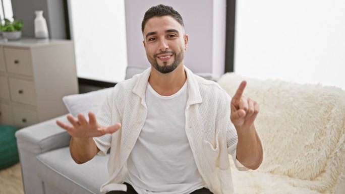 一个快乐的阿拉伯年轻人坐在家里的沙发上，用手指开玩笑地展示着6号，用他的正能量照亮了整个房间
