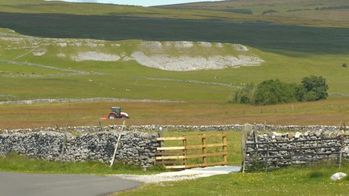 在风景秀丽的英国乡村，拖拉机在石墙草地上割草