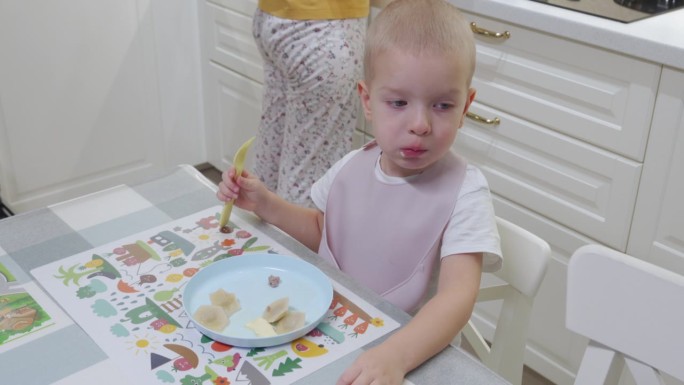 孩子小男孩坐在桌旁吃饺子，妈妈在厨房准备午饭