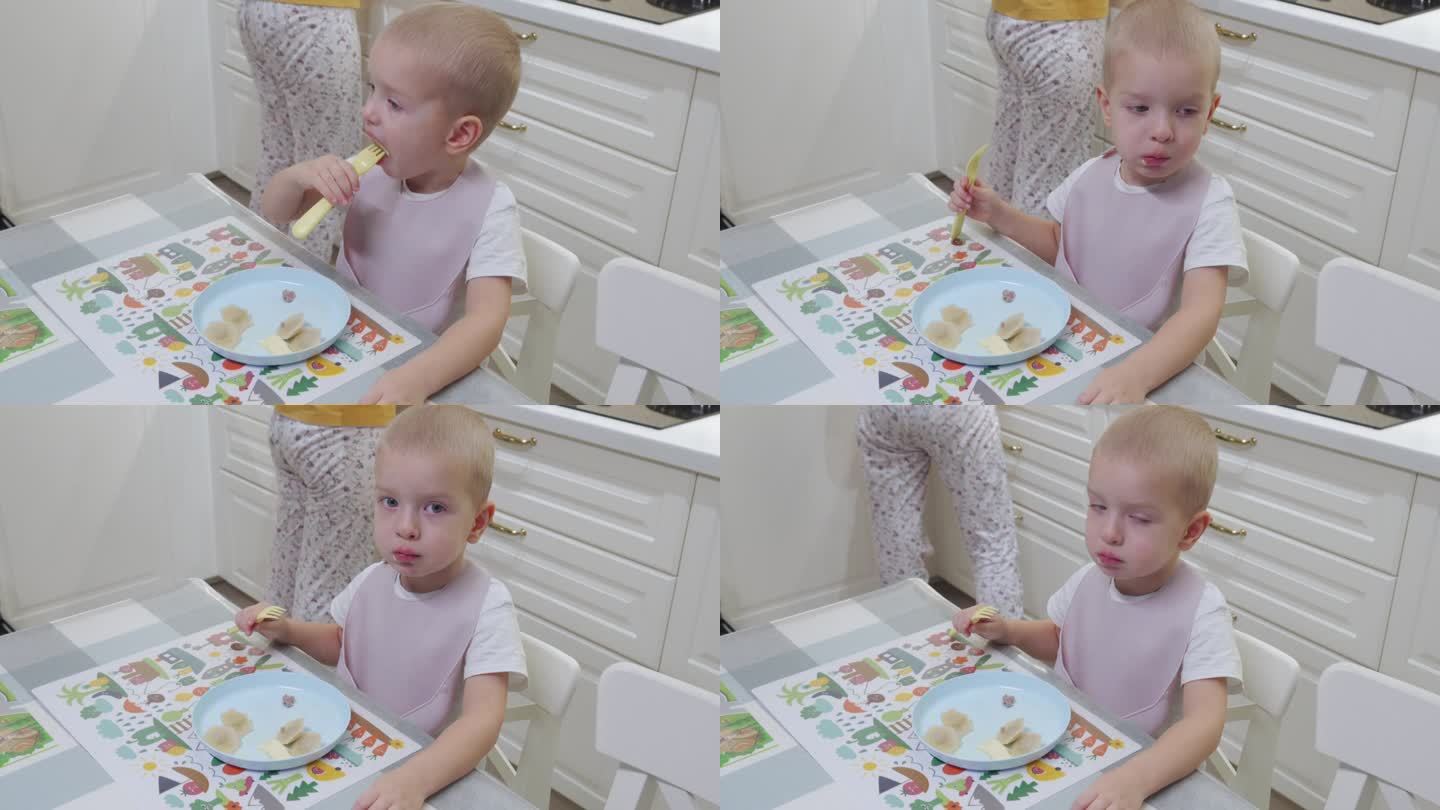 孩子小男孩坐在桌旁吃饺子，妈妈在厨房准备午饭