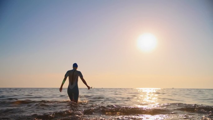 穿着潜水服的女子在日落时在海上对着天空行走的慢镜头