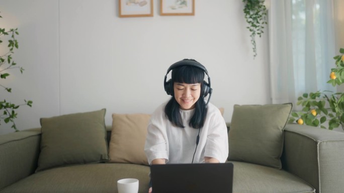 一个亚洲女人戴着耳机说话的正面照片。当时她正在家里和客户开在线会议。