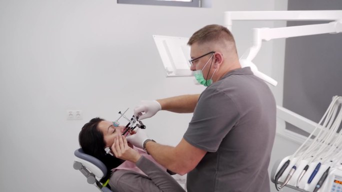 在现代牙科诊所，正畸医生在妇女脸上安装牙科面罩。牙医给女病人戴上脸罩，以获取病人的牙齿信息。现代牙科
