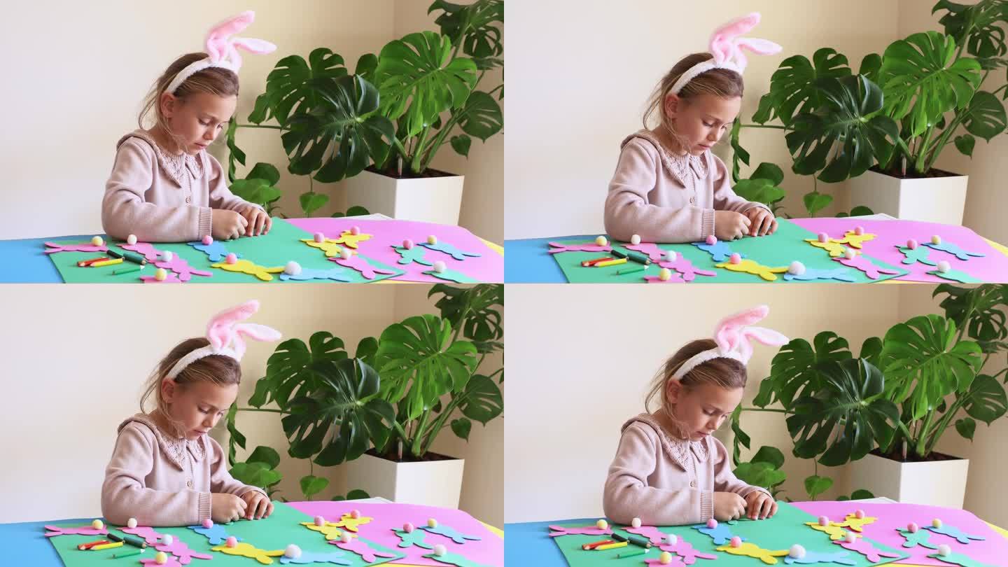 戴着兔子耳朵的小女孩正在用复活节纸制作彩色花环。可爱的儿童工艺品为复活节聚会在家里。节日艺术活动的孩