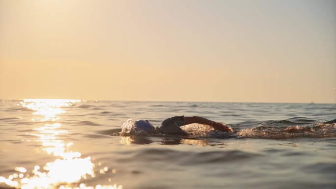 女子在夕阳下度假时在海里游泳的慢镜头镜头