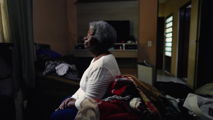 沉思的非裔美国老年妇女坐在卧室的床边，看着窗户，思考着生活。有思想的老人独自在家