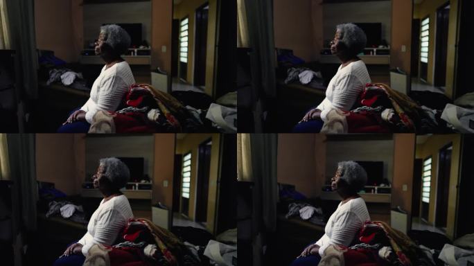 沉思的非裔美国老年妇女坐在卧室的床边，看着窗户，思考着生活。有思想的老人独自在家