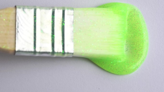 艺术家拿着画笔，画着绿色的霓虹闪光颜料的特写。在白纸上画绿线。