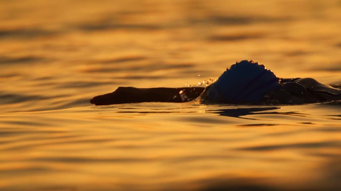 在日落时在海洋中游泳的度假女性的SLO镜头。一个女人正在海里游泳。