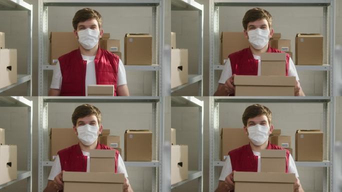 穿着红色背心的男子拿着包裹，戴着医用口罩的仓库员工在硬纸板抽屉的背景上拿着快递箱。covid期间的物
