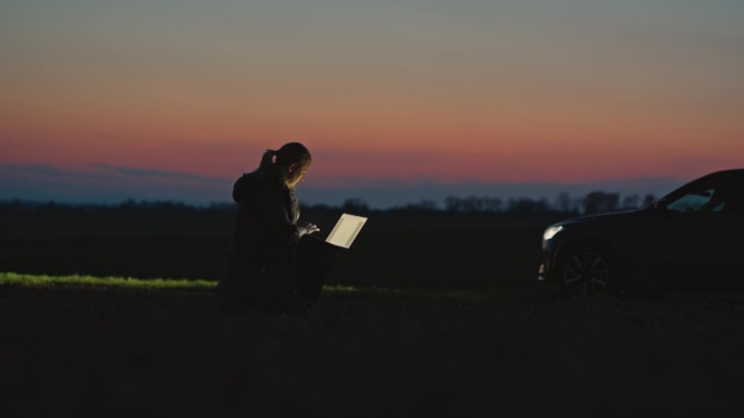SLO MO锁定镜头的女性环保人士在笔记本电脑上工作，并分析农场土壤在夕阳的天空