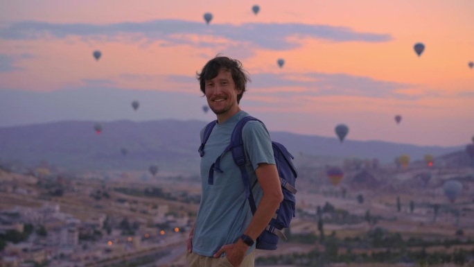 在土耳其卡帕多西亚，一名年轻的游客正在观看热气球。土耳其快乐旅行的概念。一个人站在山顶上欣赏美丽的景