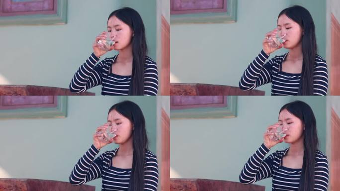 正常镜头的亚洲妇女穿着条纹衬衫喝一杯水在家里，食物和健康的概念，复制空间为文字