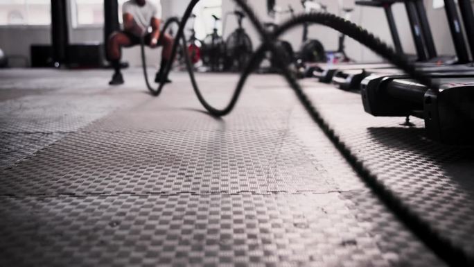 健身房里的男人，地板和战斗绳，锻炼或在健康和健康方面的高强度训练。活跃的男性，健美运动员或运动员在手