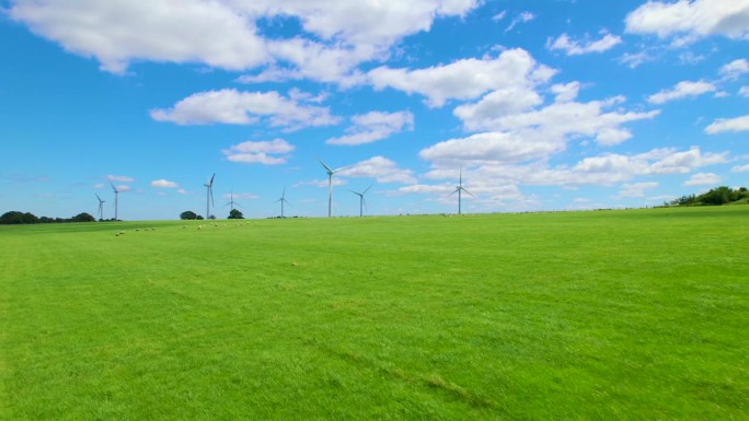 航拍:一群羊在靠近风力发电站的绿色草地上吃草