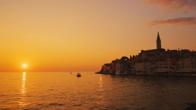 船在海上航行与古城背景在橙色的天空在日落。罗维尼，伊斯特拉，克罗地亚。