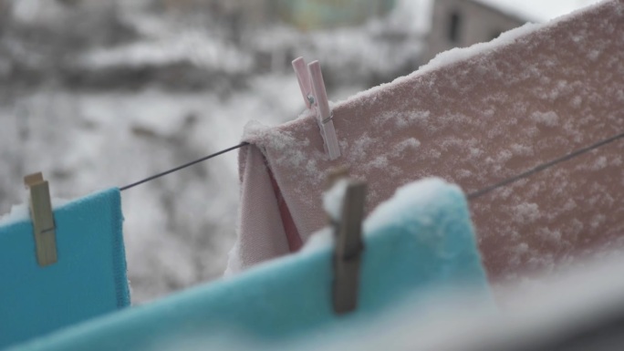 在下雪的冬天，洗好的衣服挂在户外的晒衣绳上的特写。用衣夹把洗过的衣服晾在冷的地方。蓬松的白雪挂在衣服