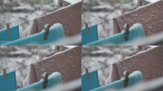 在下雪的冬天，洗好的衣服挂在户外的晒衣绳上的特写。用衣夹把洗过的衣服晾在冷的地方。蓬松的白雪挂在衣服