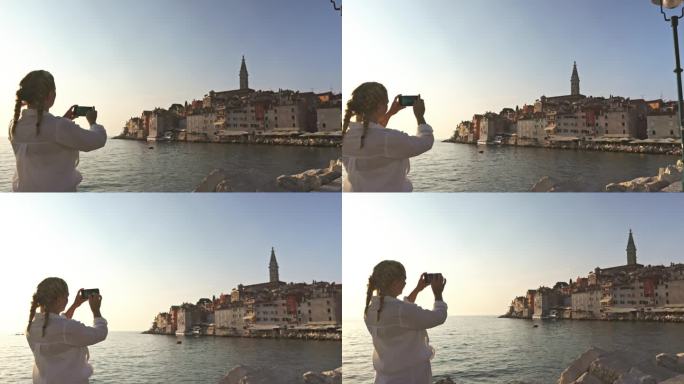 一个女人在阳光明媚的假期用智能手机拍摄古城。罗维尼，伊斯特拉，克罗地亚。