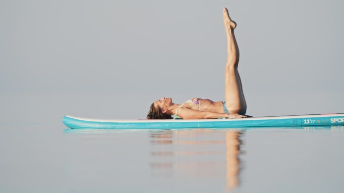 身穿比基尼的女子在海上冲浪板上进行放松练习的慢镜头