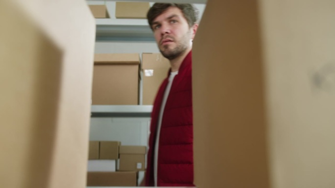 穿着红色背心的男子把包裹放在架子上，仓库的员工把快递箱放在纸板抽屉的背景上。物流、配送和仓储概念。