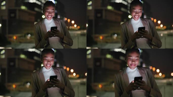 黑人女人，晚上在街上微笑着打电话，在城市里用手机打字聊天。员工，善于沟通，乐于在黑暗中与社交媒体ap