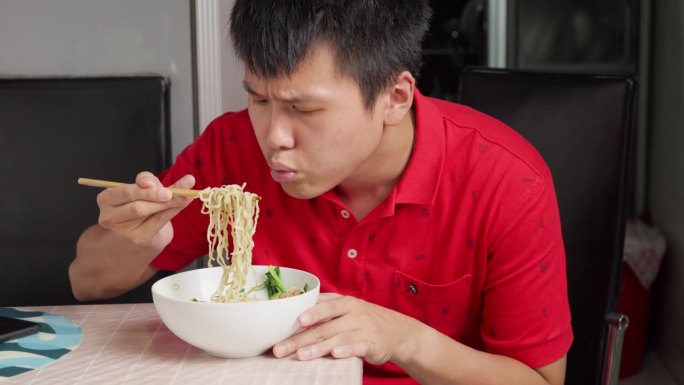 中国年轻人独自吃着巴米麦面，客厅桌上摆着画像