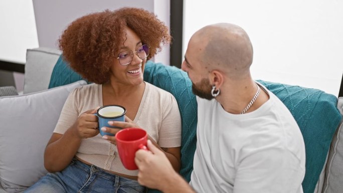 可爱的跨种族夫妇享受着早晨的咖啡，在他们客厅的家庭氛围中自信地聊天，微笑着闪烁着幸福的光芒。