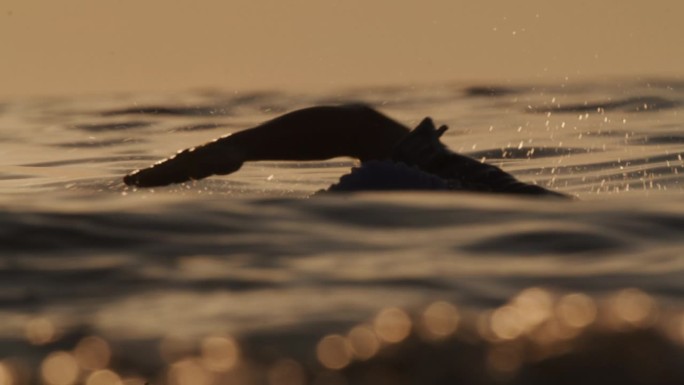 慢动作拍摄运动的女人在日落期间在海洋游泳。有目标的女人。