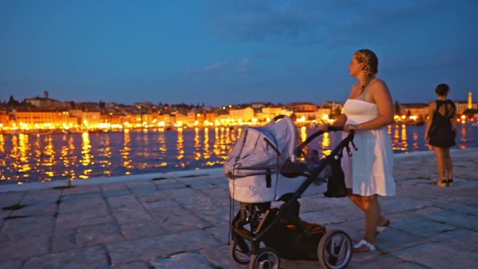 假期黄昏，女子推着婴儿车走在海边的海滨长廊上。罗维尼，伊斯特拉，克罗地亚。