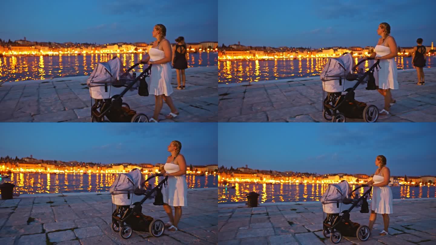 假期黄昏，女子推着婴儿车走在海边的海滨长廊上。罗维尼，伊斯特拉，克罗地亚。