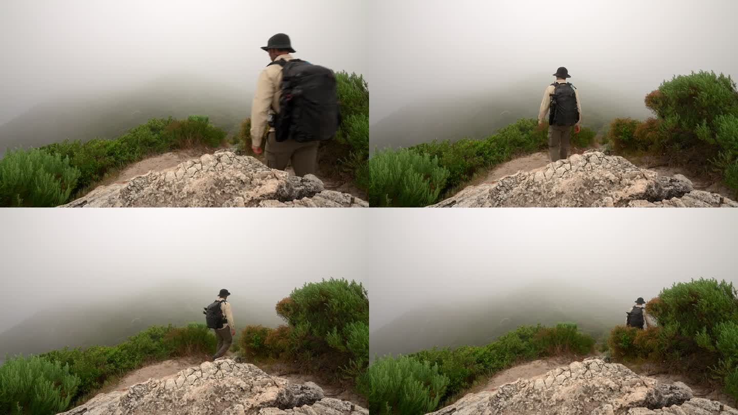 一个男人走在一条徒步小径上，转过拐角，雾气笼罩着小径。