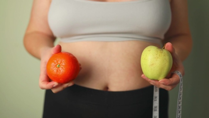 健康的有机食品，适合节食女性的概念。一个女人拿着苹果和橘子，放在健康食品前面，胳膊上还挂着一个量具。