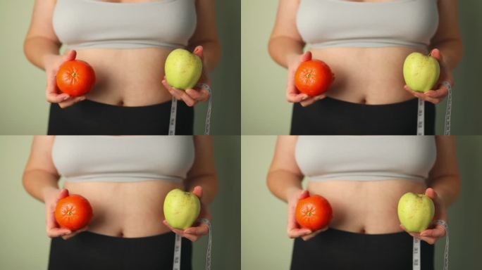 健康的有机食品，适合节食女性的概念。一个女人拿着苹果和橘子，放在健康食品前面，胳膊上还挂着一个量具。