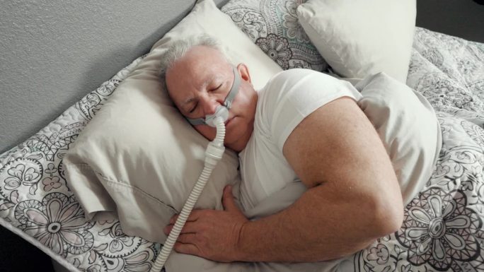 成年男子在被诊断患有睡眠呼吸暂停后使用CPAP(持续气道正压通气)机睡觉