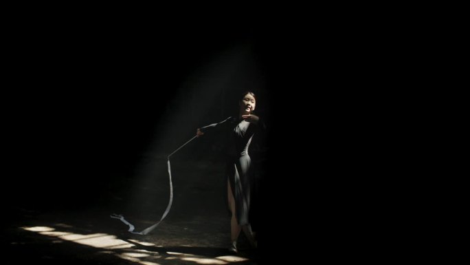 在黑暗的大厅里，芭蕾舞女演员在戏剧性的灯光下用白丝带表演的剪影。