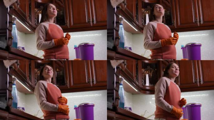 特写镜头。一位孕妇站在一个现代家庭的厨房里，环顾四周，微笑着。这个女人用戴着橡胶手套的手和叶子抚摸着
