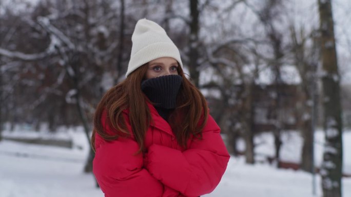 在寒冷的冬日里，穿着冬衣的年轻女子用手臂呼吸以保持温暖。悲伤冷漠的红发女人站在城市街道上
