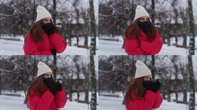 在寒冷的冬日里，穿着冬衣的年轻女子用手臂呼吸以保持温暖。悲伤冷漠的红发女人站在城市街道上