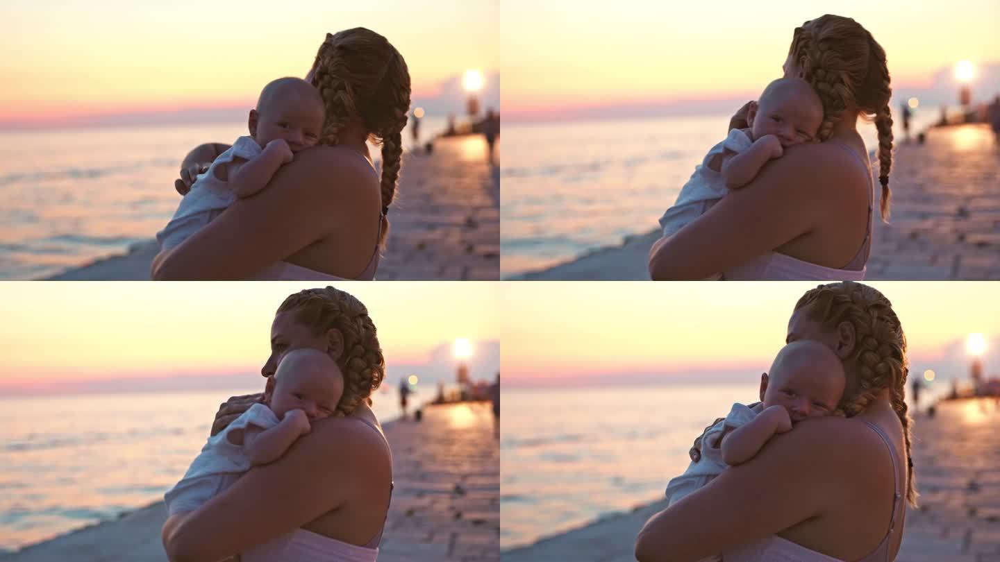 假期黄昏，母亲抱着蹒跚学步的孩子站在海边散步