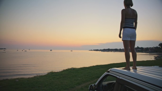 日落时站在海边露营车上的悠闲女子的慢镜头镜头