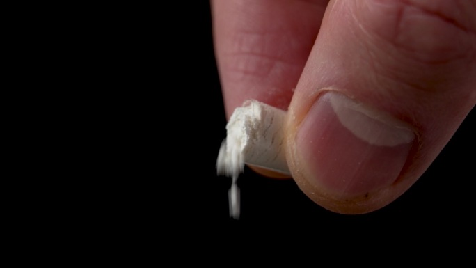 白色的药粉从手里打开的药囊里倒出来，背景是黑色的。药物与科研理念