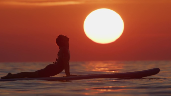 日落时在海上冲浪板上运动的女性的慢镜头镜头