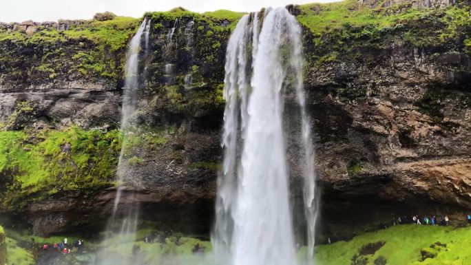 游客们聚集在冰岛的Seljalandsfoss瀑布下，倾盆大雨倾盆而下